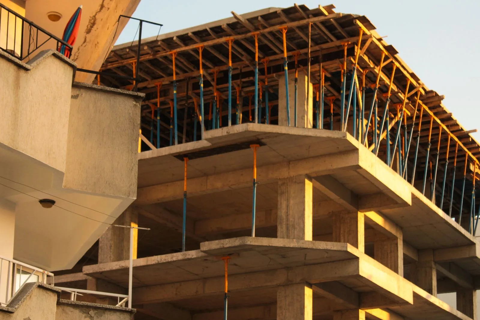 Estrutura de betão de um edifício residencial em construção, com escoras laranja e azuis sustentando a laje